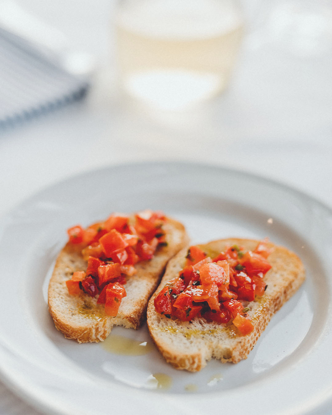 Zwei Scheiben geröstetes Brot mit gewürfelten Tomaten, Kräutern und Olivenöl auf einem weißen Teller.