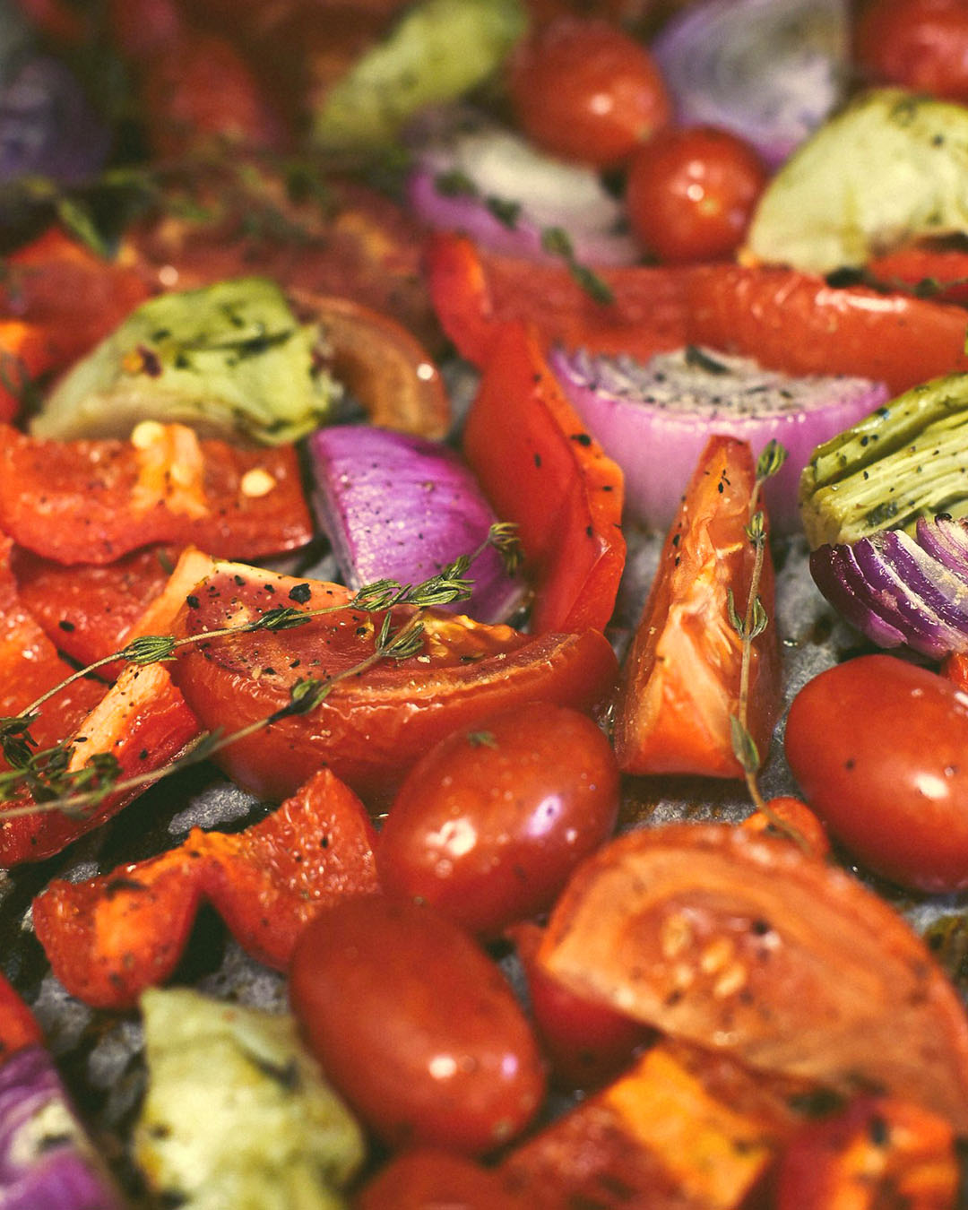 Tomatenspalten und Kirschtomaten mit roten Zwiebeln, Gemüse und frischem Thymian auf einem Backblech.