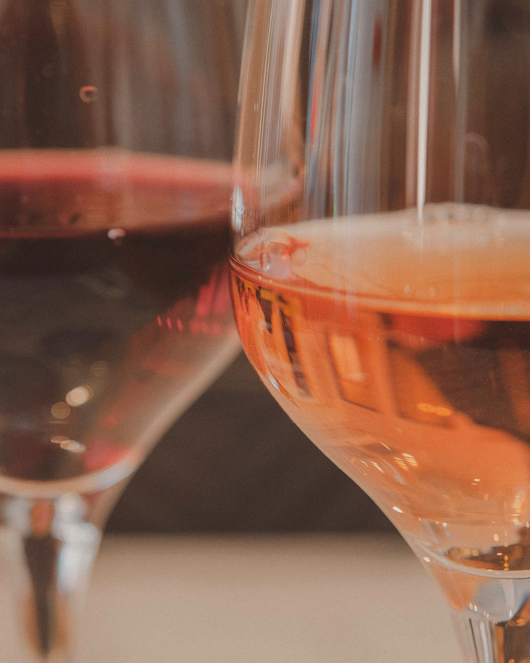 Nahaufnahme zweier Weingläser mit Rotwein und Roséwein vor einem warmen, unscharfen Hintergrund.